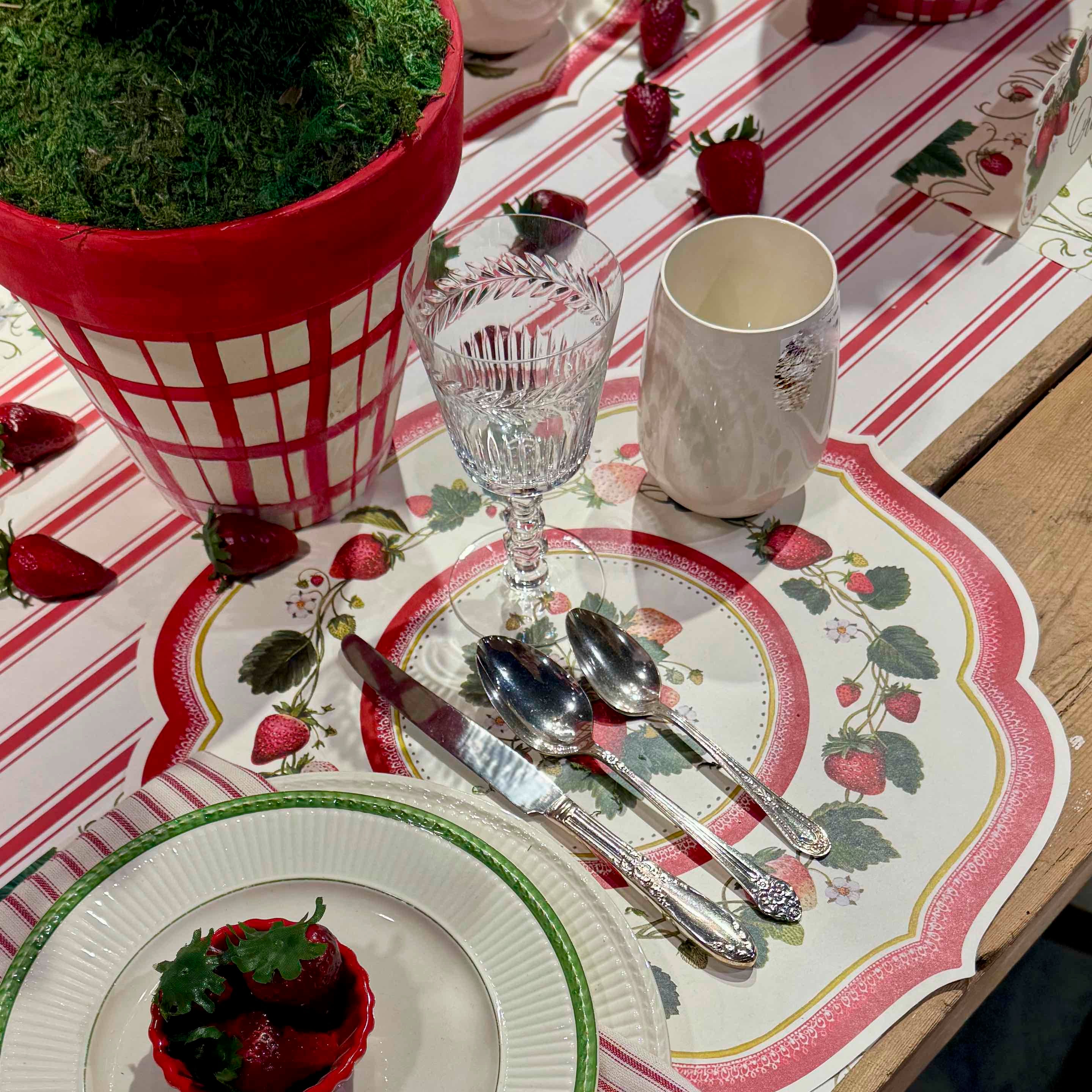 Dining table setting with strawberry-themed placemats, glasses, and cutlery.