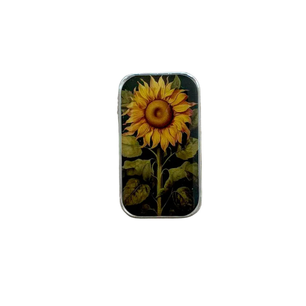 A small rectangular metal tin with a sunflower illustration on the lid, placed on a light wood surface.