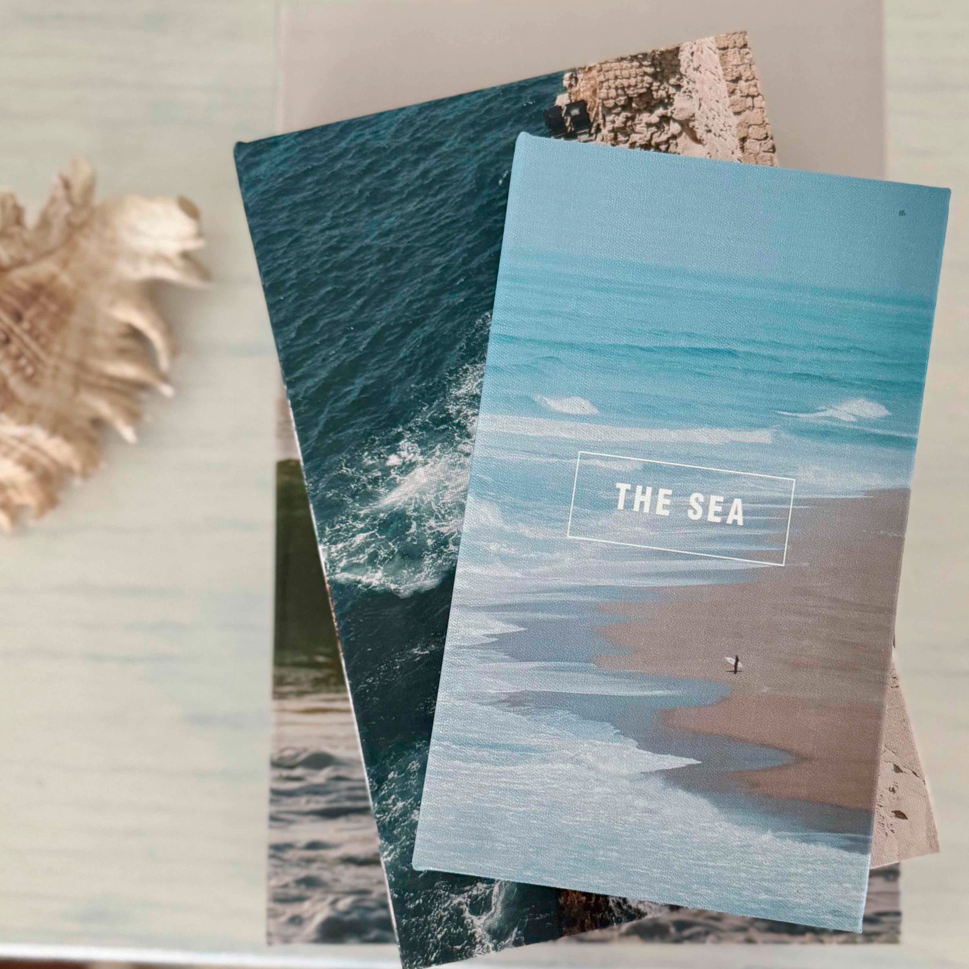 Two notebooks with ocean-themed covers on a light surface.