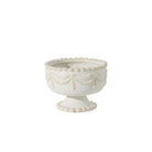 An off-white ceramic pedestal bowl with embossed classical drapery and beaded detailing on the rim, set against a plain white background.