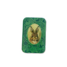 A rectangular green tin with rounded corners, featuring a central oval illustration of a brown rabbit surrounded by dark green floral and vine patterns, placed on a light wood surface.