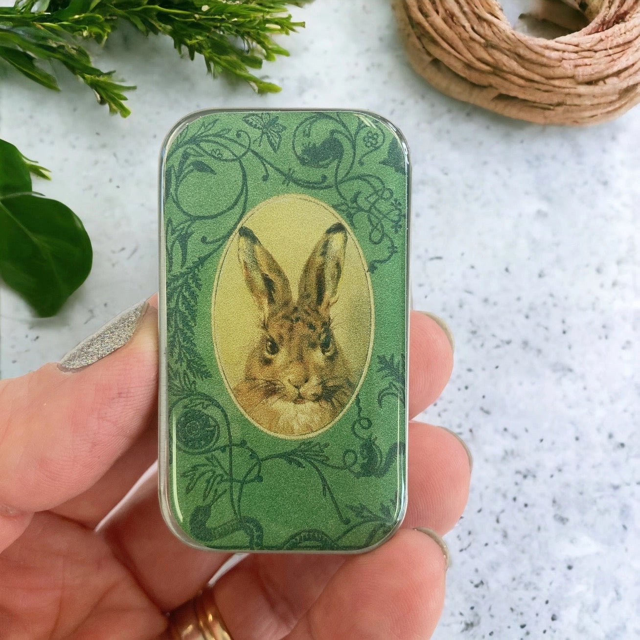 Hand holding a small green tin with a rabbit illustration on a light background