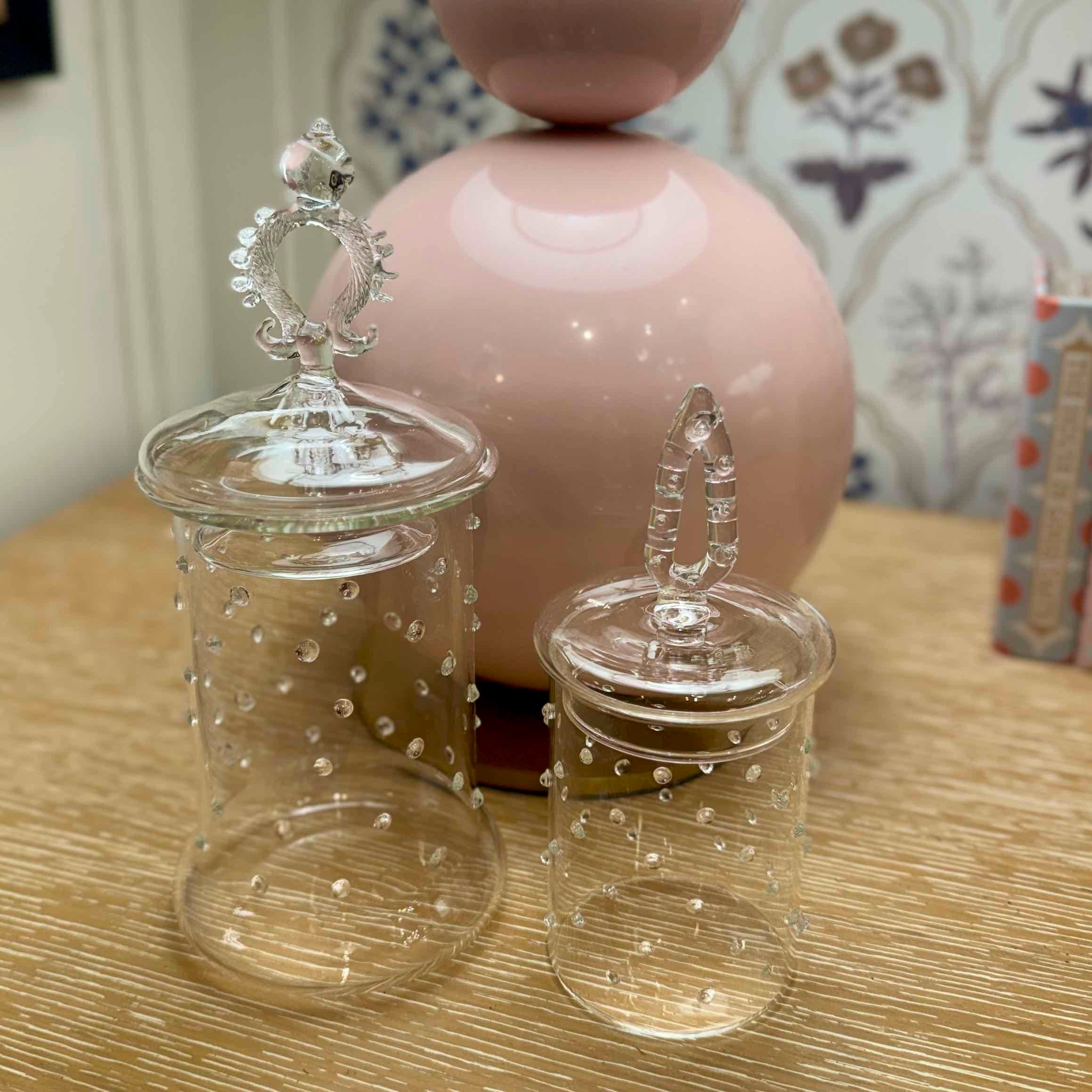 Two clear glass jars with decorative lids on a wooden surface.