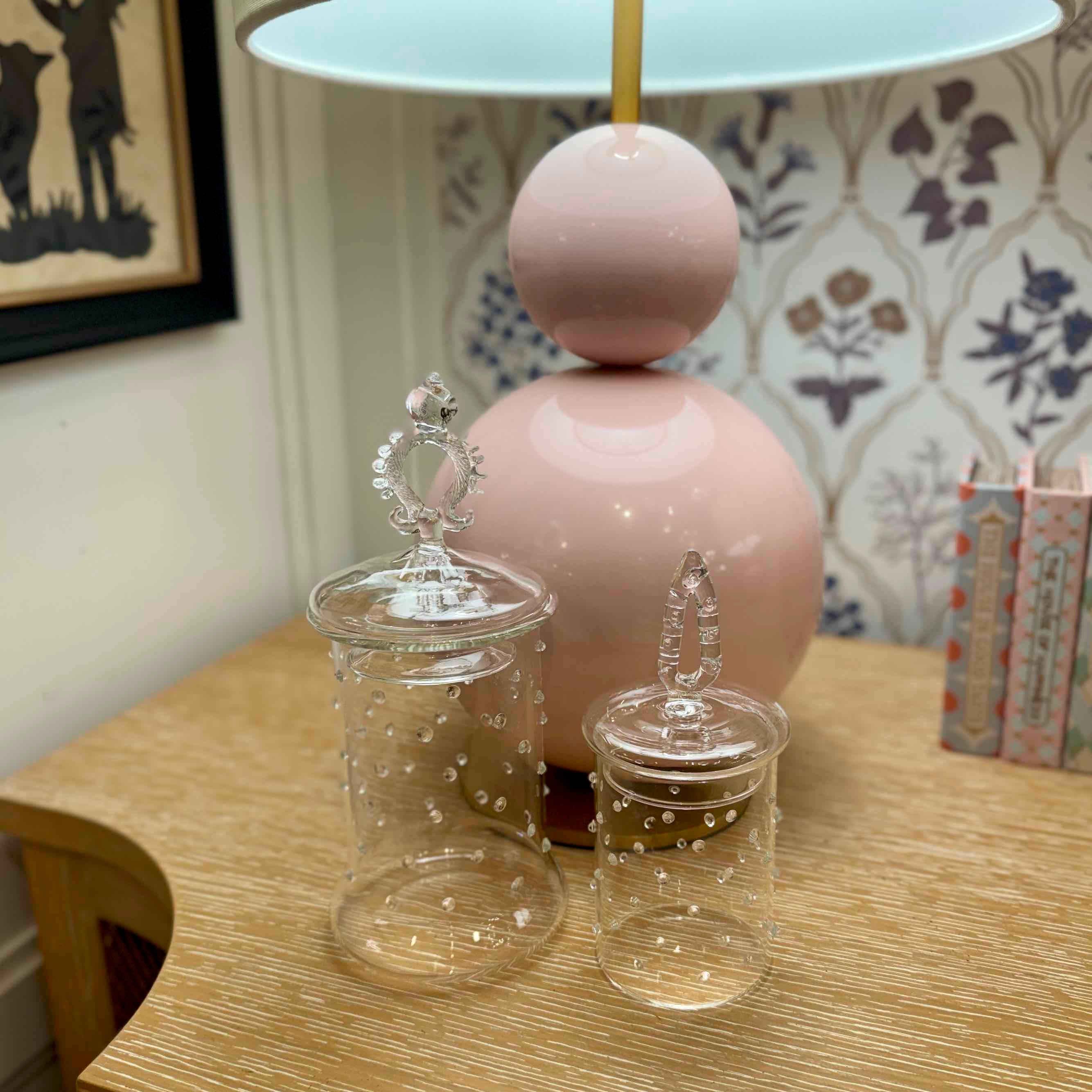 Decorative glass jars with a pink lamp in the background on a wooden surface.