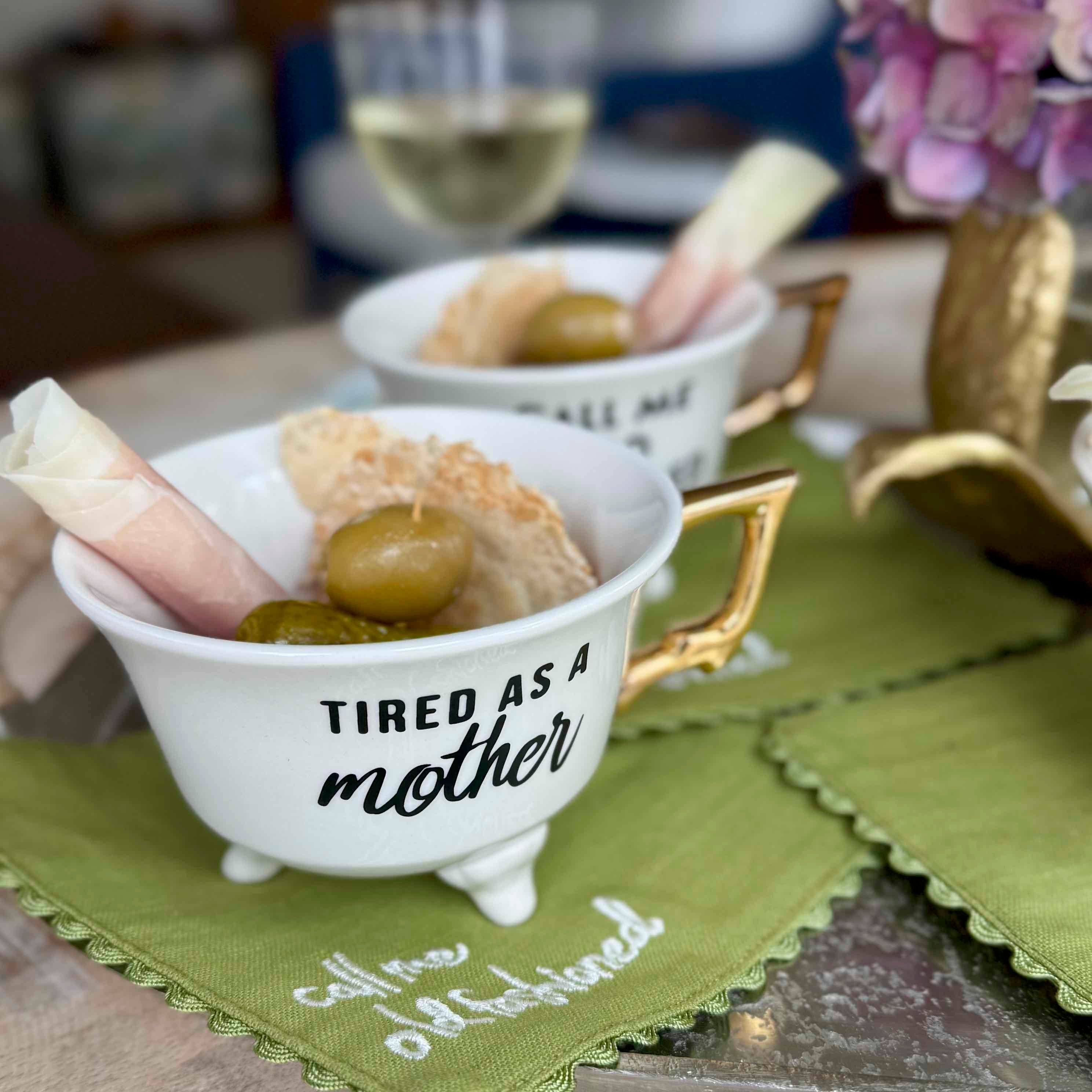 White bowl with olives and bread on a green napkin with text, blurred background