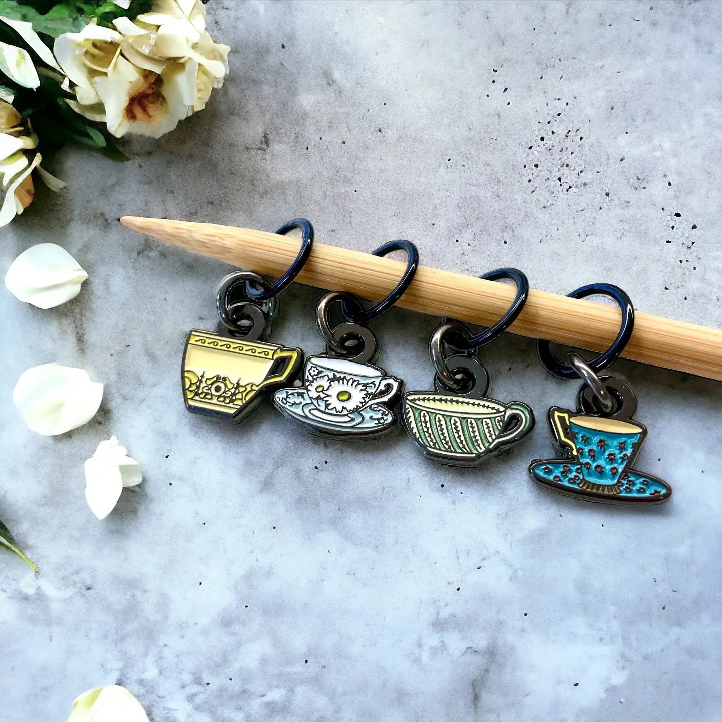 Set of tea cup-shaped charms on a wooden knitting needle with flowers in the background