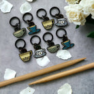 Tea cup keychains on a gray surface with wooden sticks and flowers.