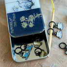 Tin box with decorative keychains featuring teacups and flowers on a wooden surface.