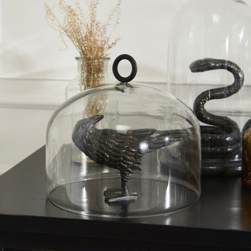 Decorative black bird figure under a glass dome on a table.