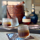 Two glasses of whiskey on a coaster with bottles in the background