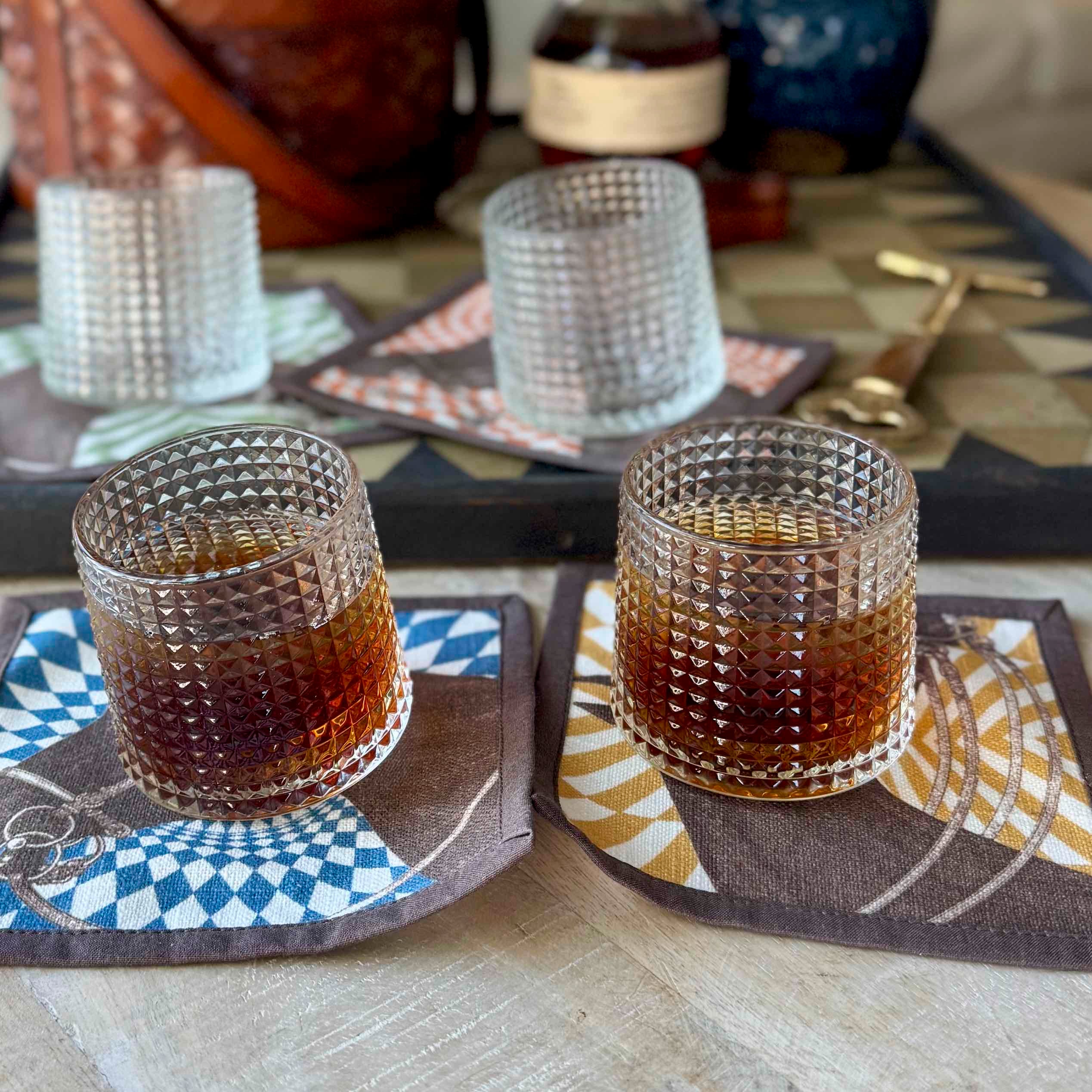 Two glass tumblers with a layered drink on patterned coasters.