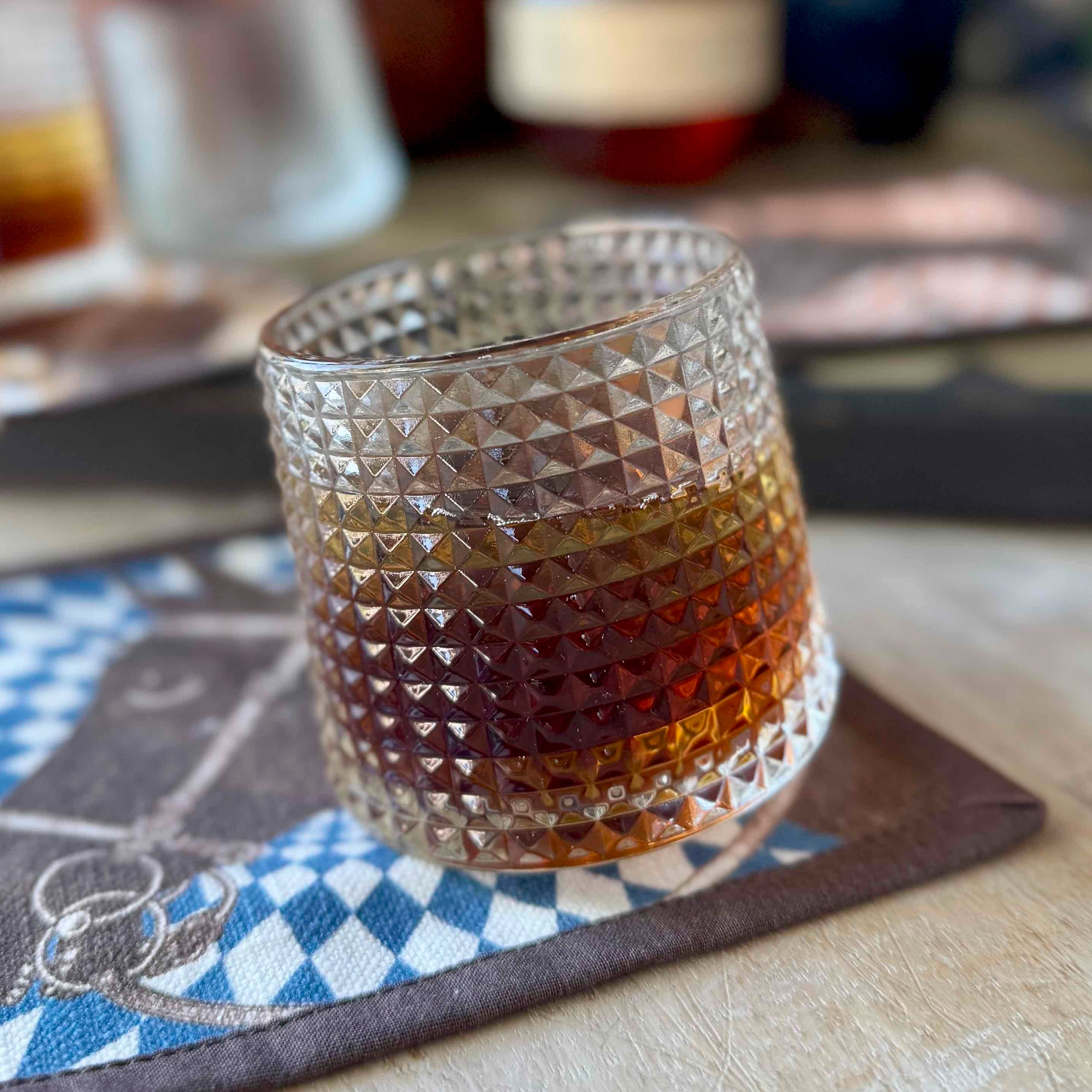 Glass with a textured pattern filled with a layered drink on a checkered mat.