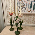 Decorative candle holders with candles on a surface, with a floral-patterned wall in the background.