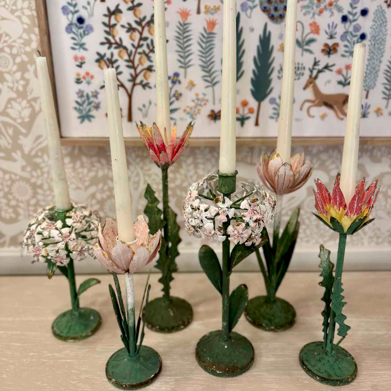 Decorative candle holders shaped like flowers on a wooden surface with a floral-patterned wall in the background.