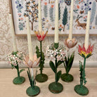 Decorative candle holders shaped like flowers on a wooden surface with a floral-patterned wall in the background.