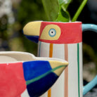 Colorful ceramic pitcher with abstract design against a blurred green background