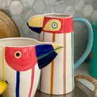 Colorful ceramic pitcher and mug with bird design on a kitchen counter.