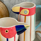 Two ceramic bird-shaped pitchers with colorful designs on a neutral background