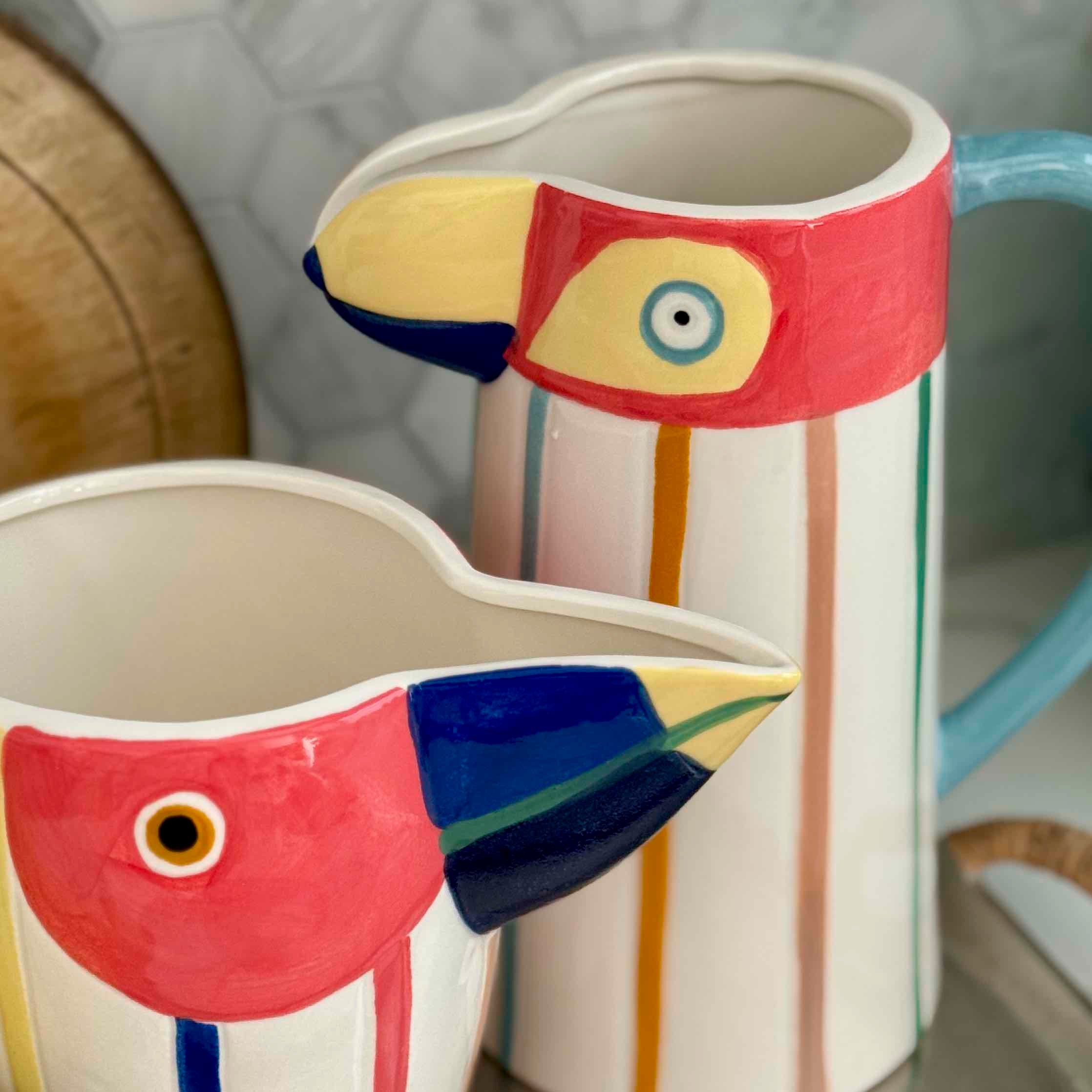 Two ceramic bird-shaped pitchers with colorful designs on a neutral background