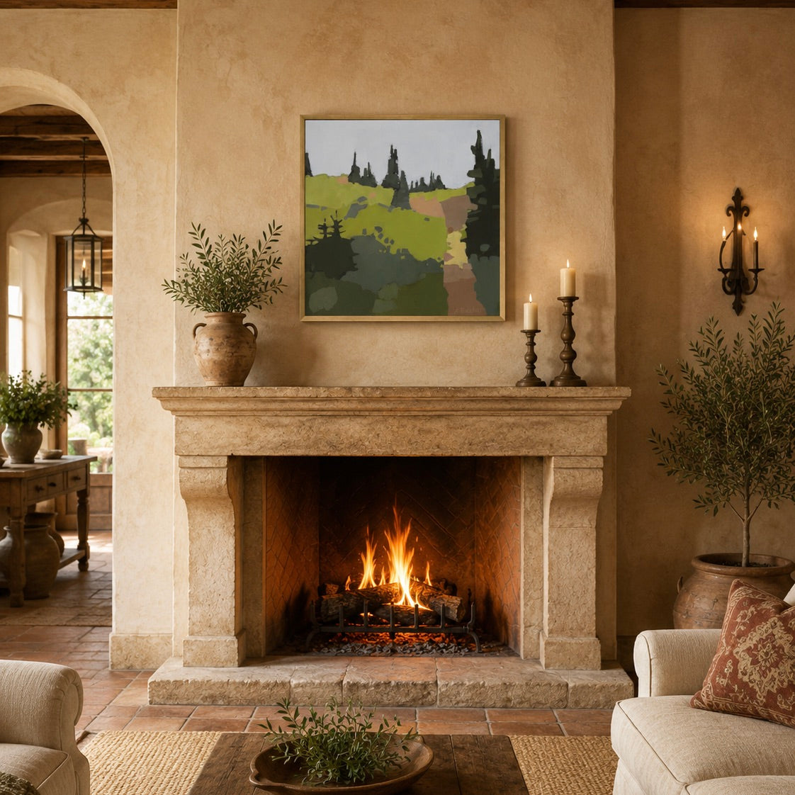 A framed landscape art print hangs on a beige plaster wall above a stone fireplace in a warm, rustic living room. The print depicts rolling green hills and dark pine trees under a soft gray sky.