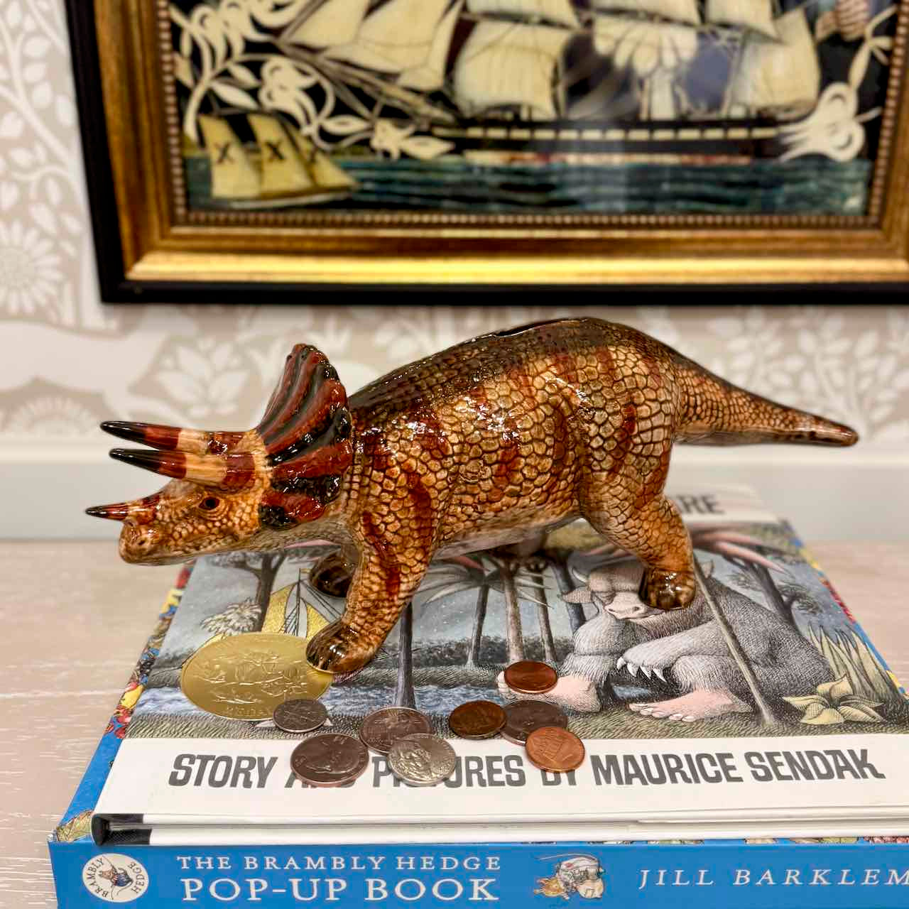 Triceratops dinosaur toy on a book with a framed picture of a ship in the background