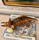 Dinosaur toy on top of a book with a gold frame in the background