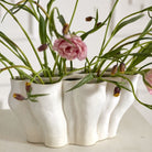 White ceramic planter with green plants and pink flowers on a white surface