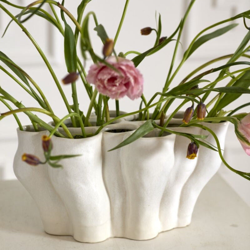 White ceramic planter with green plants and pink flowers on a white surface