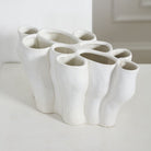 A white, sculptural ceramic planter with multiple organic-shaped cup-like openings, photographed on a light surface against a soft white background.