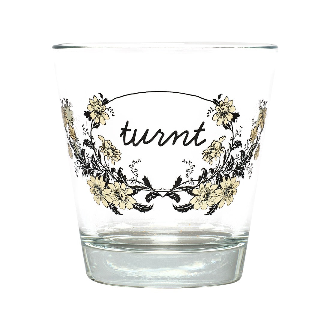 A clear glass tumbler with a floral wreath design and the word 'turnt' in black script on the front, shown against a plain white background.