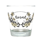 A clear glass tumbler with a floral wreath design and the word 'turnt' in black script on the front, shown against a plain white background.