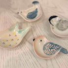 Four small bird-shaped ceramic dish holders with blue and yellow floral patterns, arranged on a light wood surface.