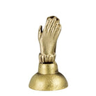 A small metallic gold figurine of a praying hand on a round base, photographed against a plain white background.