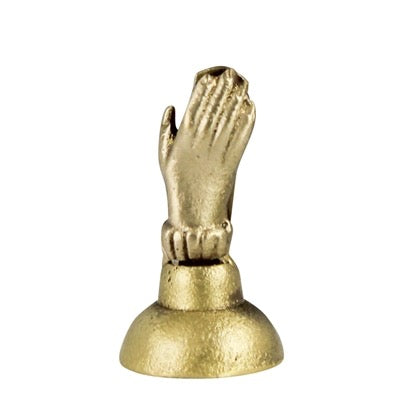 A small metallic gold figurine of a praying hand on a round base, photographed against a plain white background.