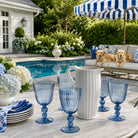 Outdoor setting with blue glasses, a white pitcher, and dogs on a couch by a pool.