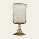 A clear glass with vertical etched laurel leaves design on it, standing on a solid base.