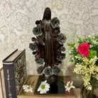 Statue of a religious figure with floral elements on a table with books and flowers.
