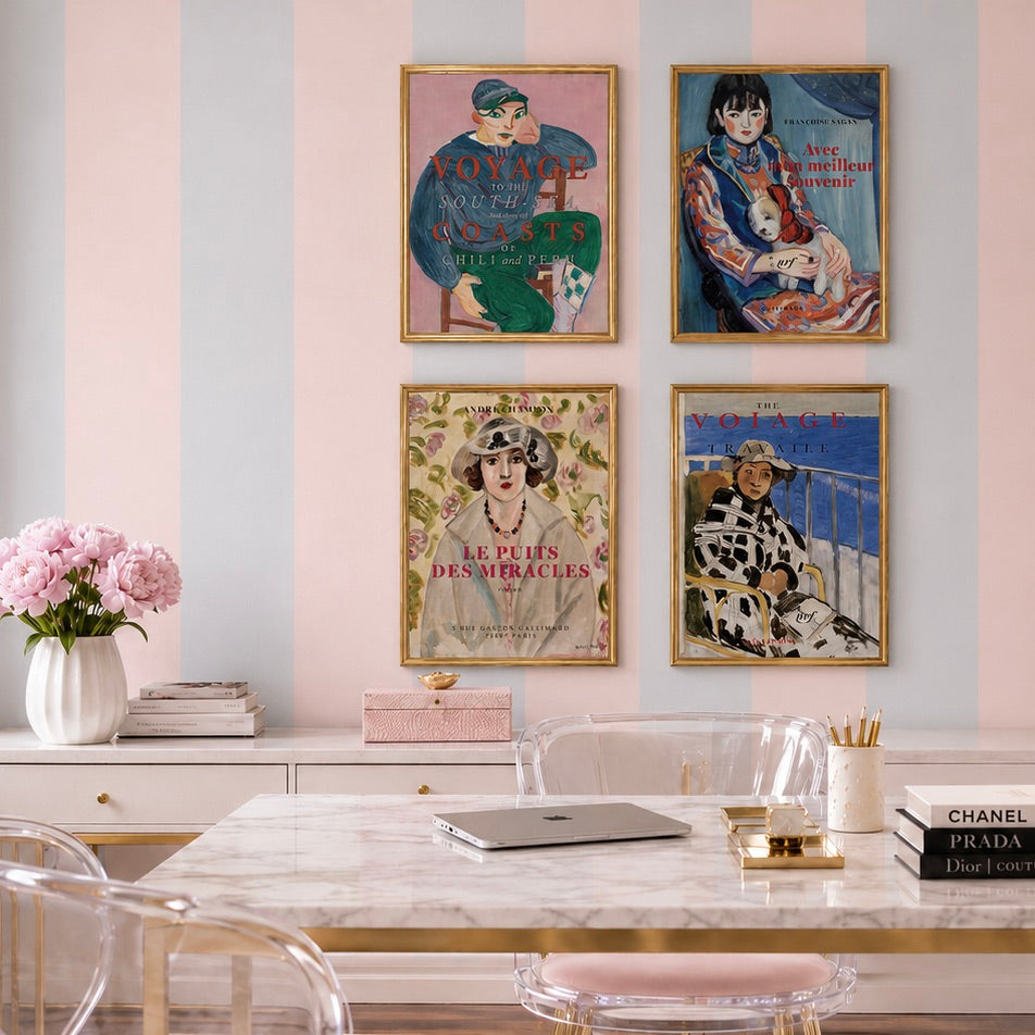 Four framed vintage-style fashion art prints with French text are displayed on a pink and white striped wall above a marble dining table in a styled room setting.