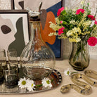 Decorative setting with a glass decanter, flowers, and decorative items on a table.