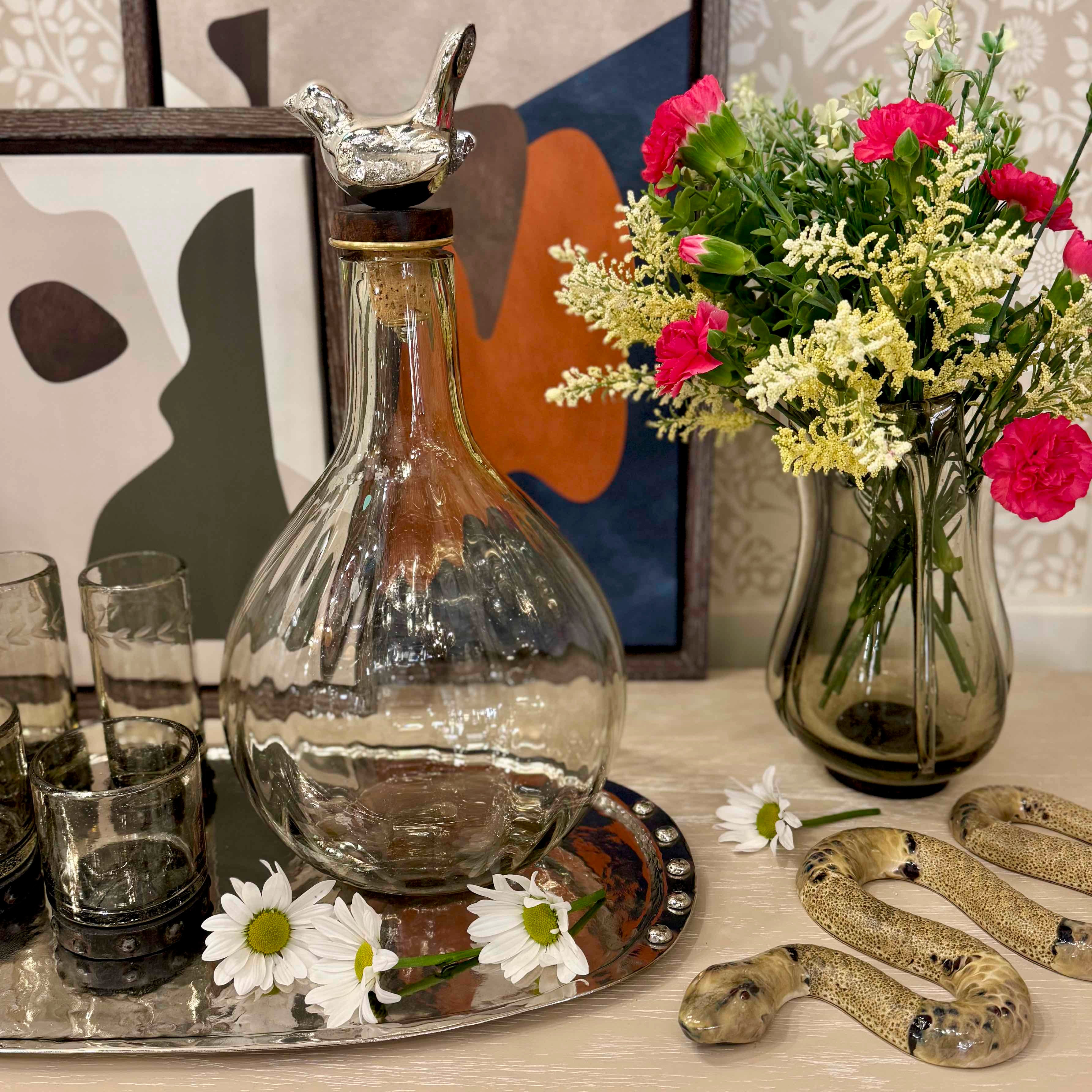 Decorative setting with a glass decanter, flowers, and decorative items on a table.