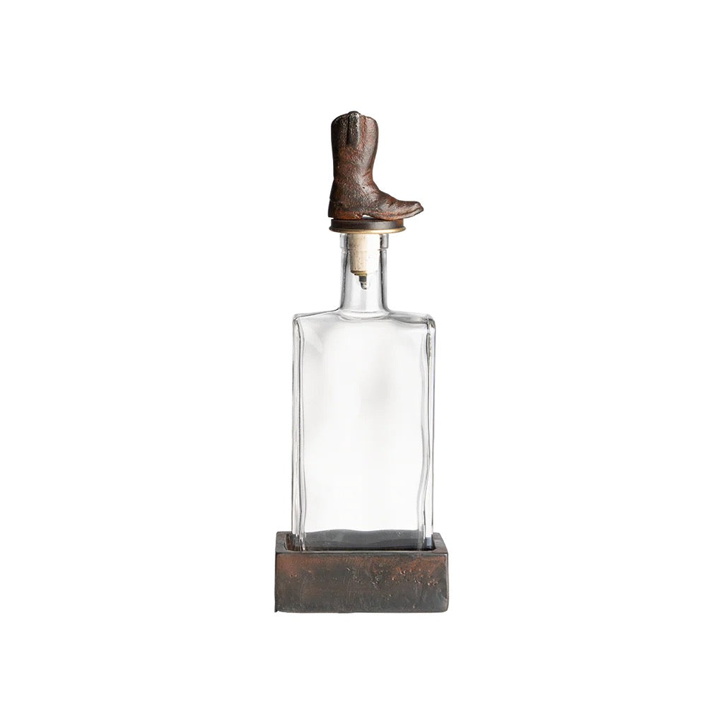 Clear glass decanter with a rustic brown boot on top against a white background