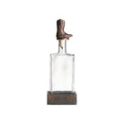 Clear glass decanter with a rustic brown boot on top against a white background