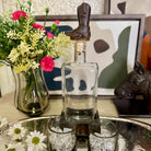 Decorative setting with a glass decanter, cowboy boot, and flowers on a table.