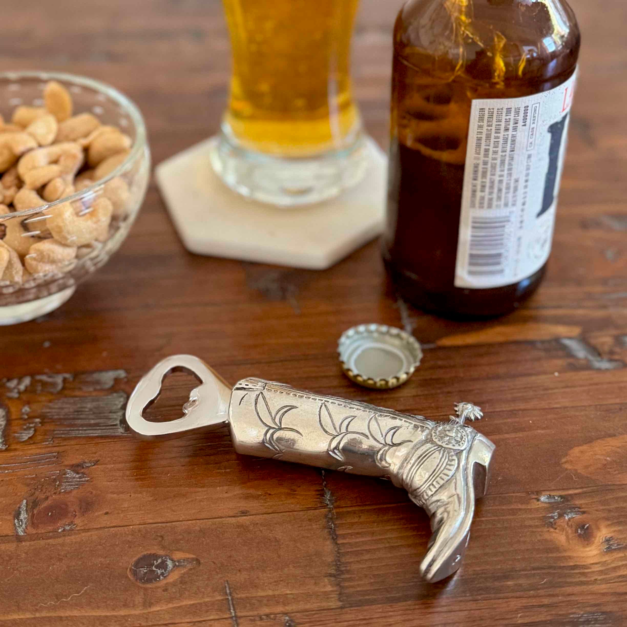 Cowboy boot bottle opener on a wooden surface with a beer bottle and glass in the background.