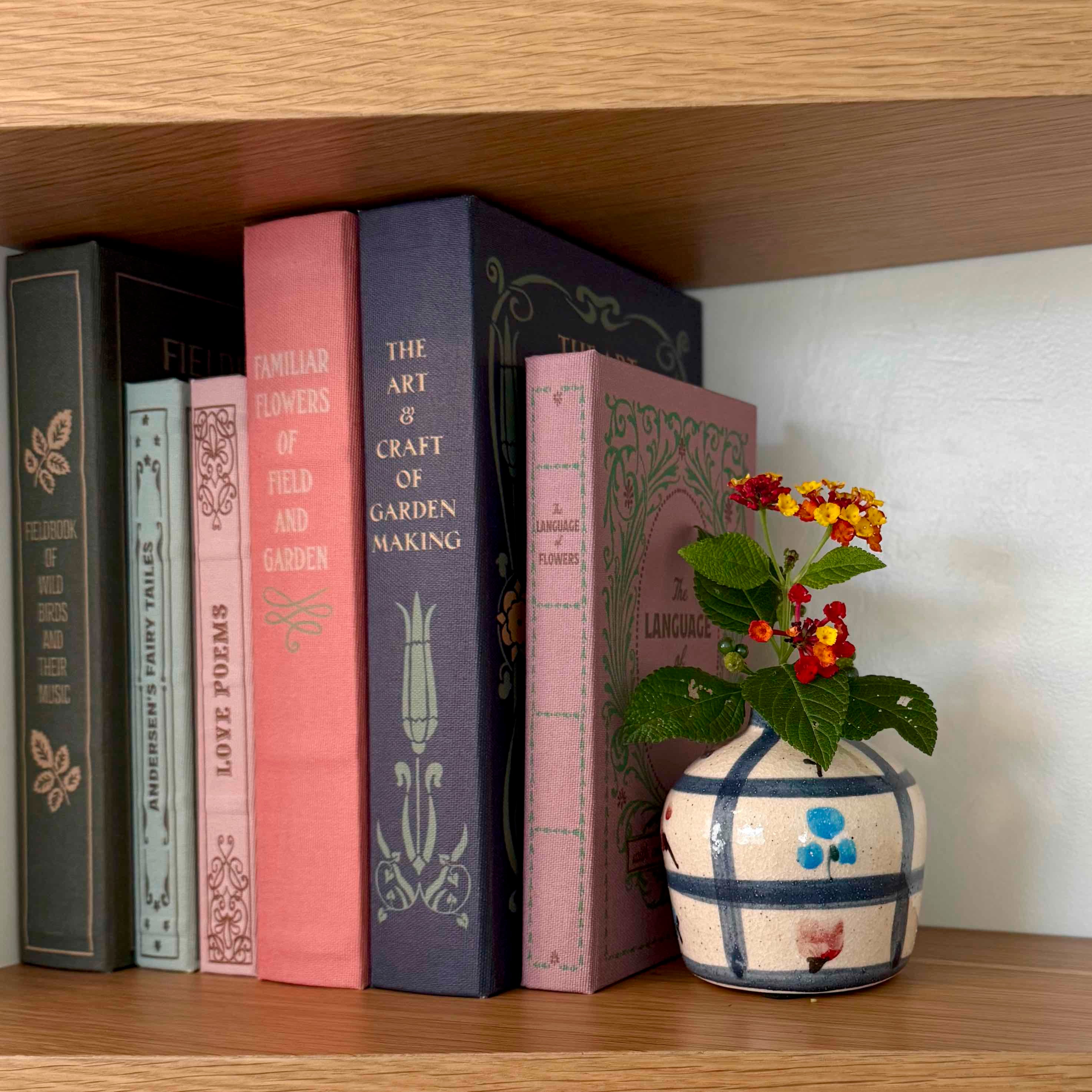 Bookshelf with decorative books and a vase with flowers on a wooden surface.