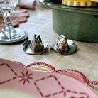 Two silver salt shakers on a table with a green pot and glass in the background.