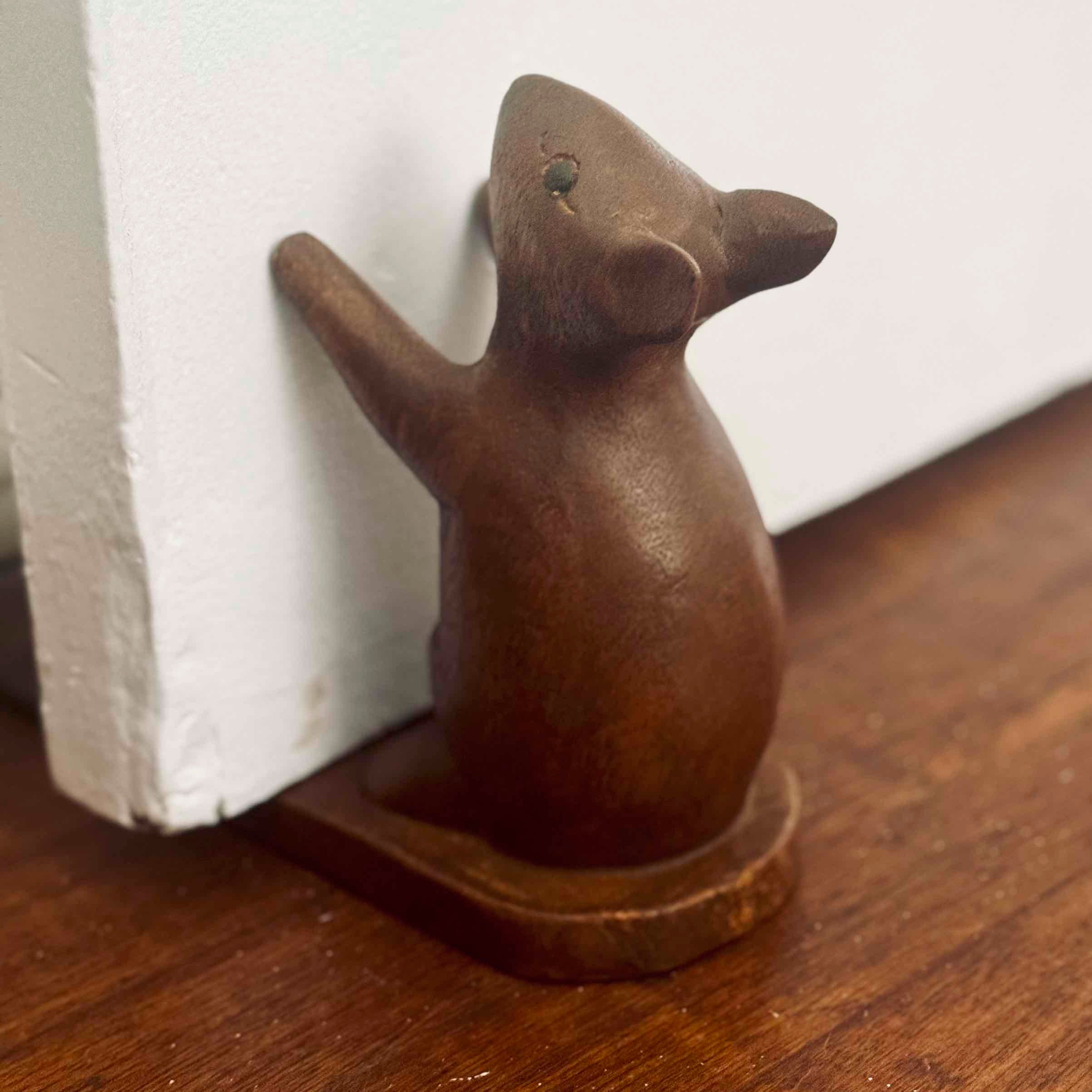 Wooden mouse door stopper on a wooden surface with a white baseboard in the background