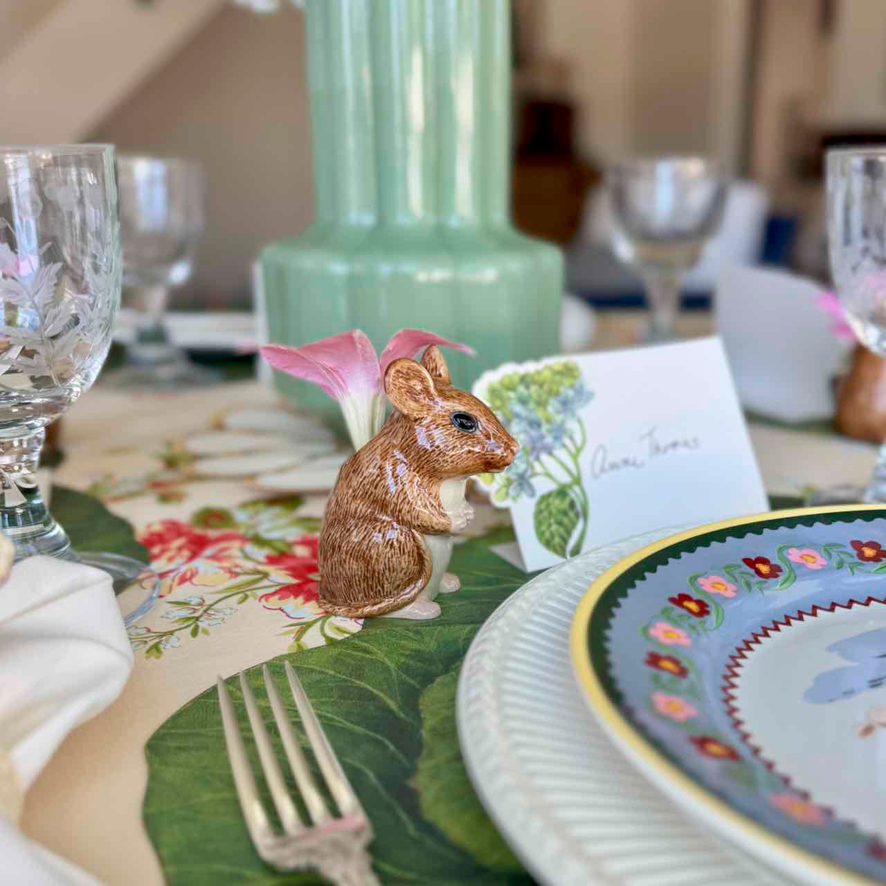 Decorative table setting with a small animal figurine on a floral place mat.
