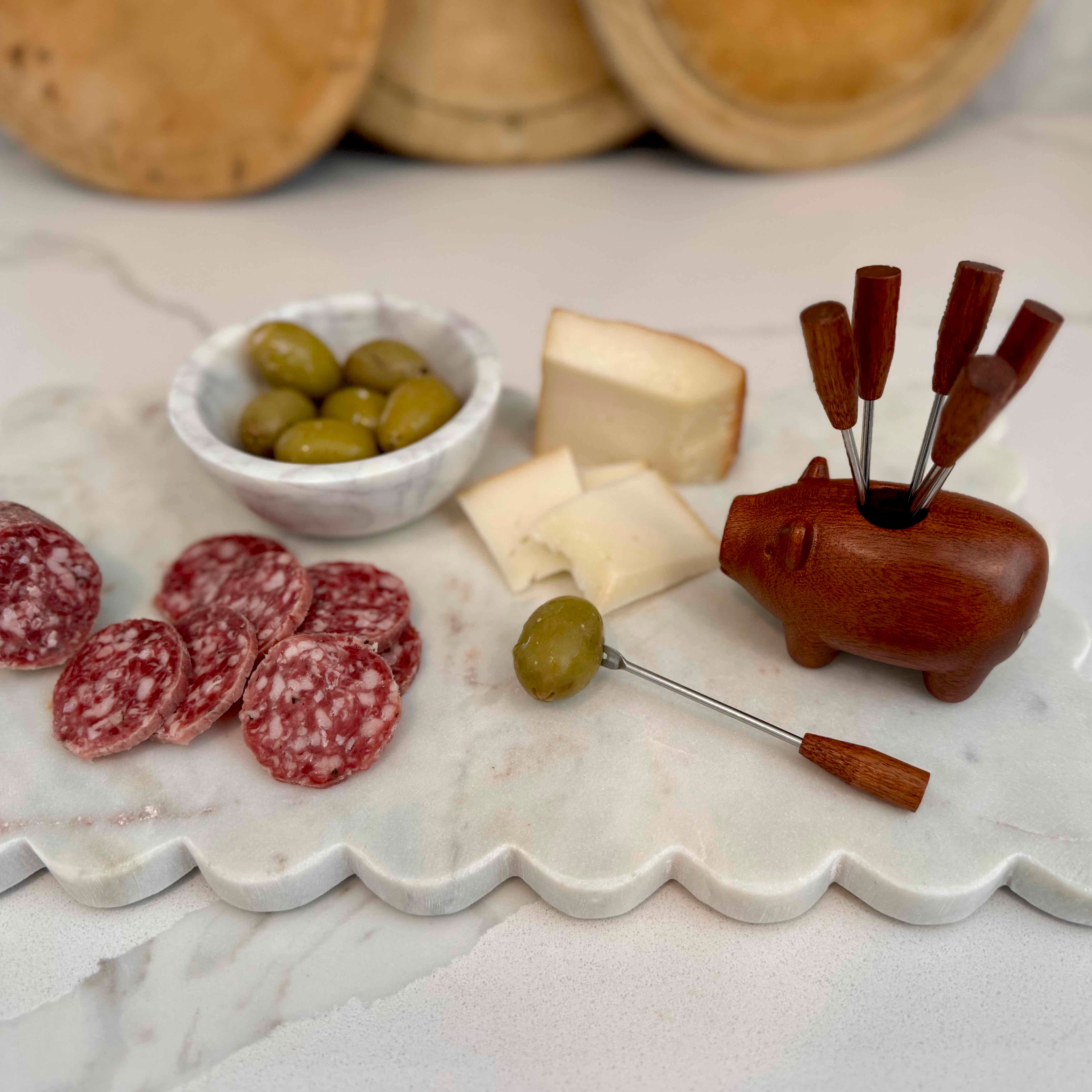 Platter with cured meats, olives, and cheese alongside a wooden pig-shaped cheese knife set.