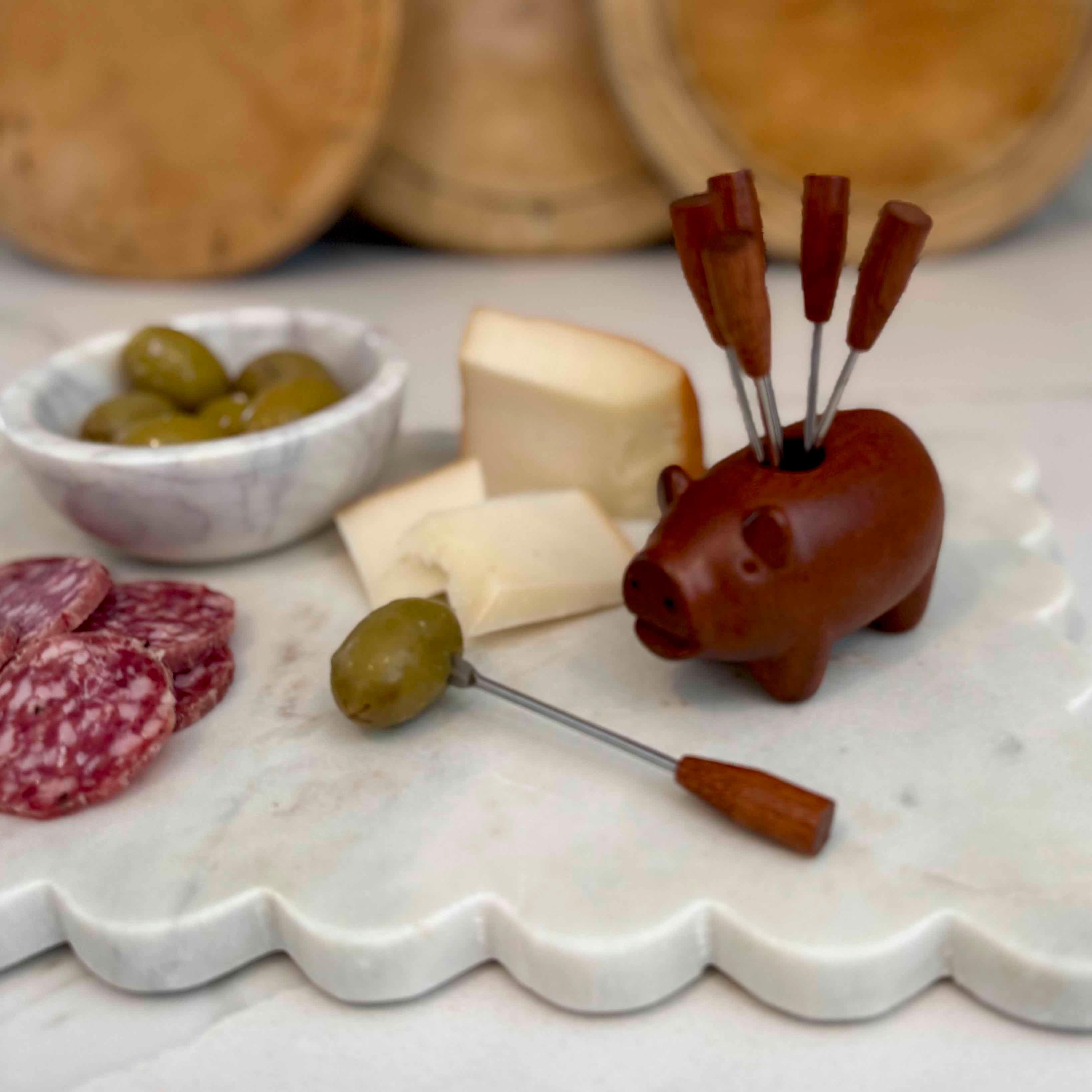 Pig-shaped olive pick with olives and cheese on a marble surface